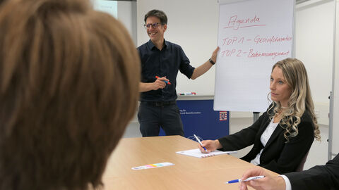 Ausbildung höherer Dienst Eine Person an einem Flipchart, drei Personen sitzend an einem Tisch, sich Notizen machend