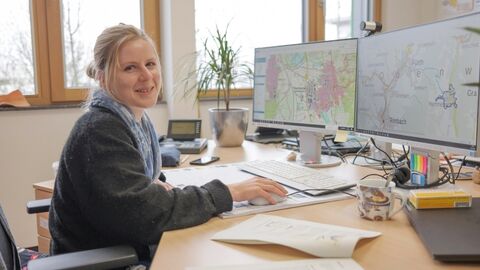 Ausbildung Geomatik Junge Frau am Schreibtisch vor zwei Monitoren, Blick in Richtung Kamera